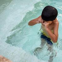 feliz indiano Garoto natação dentro uma piscina, criança vestindo natação traje ao longo com ar tubo durante quente verão Férias, crianças Garoto dentro grande natação piscina. foto