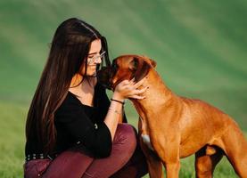 garota amando seu cachorro boxer no prado verde foto