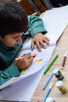 inteligente indiano pequeno Garoto executar polegar pintura com diferente colorida água cor kit durante a verão Férias, fofa indiano criança fazendo colorida polegar pintura desenhando em de madeira mesa foto
