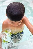 feliz indiano Garoto natação dentro uma piscina, criança vestindo natação traje ao longo com ar tubo durante quente verão Férias, crianças Garoto dentro grande natação piscina. foto