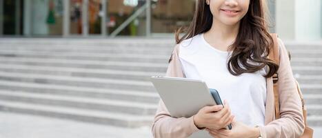 bela estudante mulher asiática com mochila e livros ao ar livre. menina sorriso feliz carregando um monte de livro no campus da faculdade. retrato feminino na universidade internacional da ásia. educação, estudo, escola foto