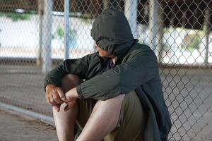 homem desgasta moletom com capuz estava detido dentro metal internet jaula, senta em a chão. conceito, delinquência. punição. detenção.criminosos. sem liberdade. esperando para liberdade. foto