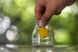 uma mão colocar amarelo Estrela para uma vidro jarra para voto ou satisfação serviço. foto