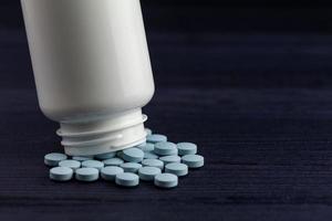 frasco de medicamento e pílulas azuis derramado sobre fundo azul de madeira. drogas farmacêuticas. foto