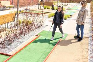 mãe e filha desfrutando juntos jogando mini golfe dentro a cidade. foto