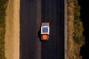 pesado vibração rolo às trabalhos pavimentação asfalto, estrada reparando. estrada rolo achatamento Novo asfalto. aéreo Visão foto