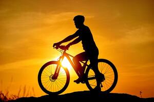 silhueta homem e bicicleta relaxante em embaçado nascer do sol céu fundo foto