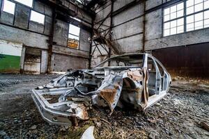 abandonado dentro a esvaziar construção a velho oxidado táxi do a passageiro carro. a quadro, Armação do estragado carro em a terra dentro a grande desolado fábrica foto