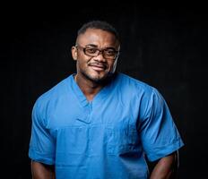 sorridente africano americano homem posando. homem dentro óculos com muscular corpo tipo vestindo médico uniforme. foto