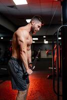 bonito muscular fisiculturista com nu tronco fazendo exercício em tríceps. jovem saudável homem Treinamento Difícil às academia. foto