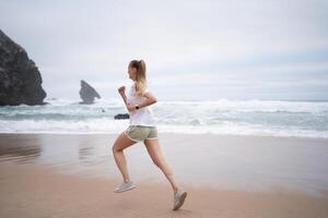 desportivo jovem mulher corrida em arenoso de praia ao longo mar foto