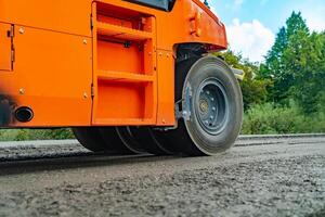 laranja estrada rolo faz a pavimentação. fechar Visão em a estrada rolo trabalhando em a estrada construção local. estrada maquinaria foto