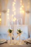 dois esvaziar Casamento champanhe óculos com cremoso arcos e flor decoração em a mesa. óculos para noivo e noiva. foto