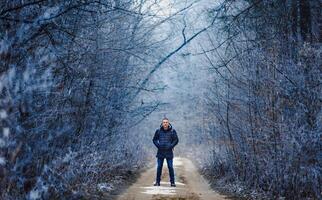 bonito homem dentro inverno pano em pé dentro parque e olhando às Câmera. neve coberto árvores parque dentro inverno. gelado temporada. foto