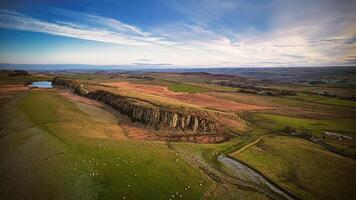 aéreo Visão do uma campo estrada às pôr do sol com exuberante verde Campos e uma macio, colorida céu às sicômoro brecha, Northumberlândia, Reino Unido. foto