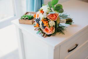 nupcial ramalhete do branco e laranja flores em uma branco mesa. Casamento acessórios do a noiva foto