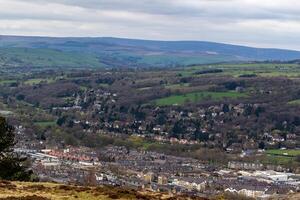 cênico Visão do uma Cidade aninhado dentro uma exuberante vale com rolando colinas dentro a fundo debaixo uma nublado céu dentro Ilkley, yorkshire foto