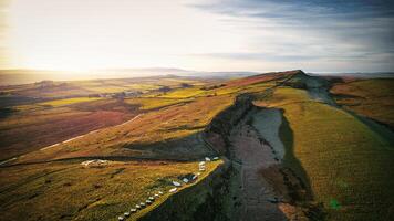 aéreo Visão do uma enrolamento estrada através uma exuberante, rolando panorama às nascer do sol, com caloroso luz fundição grandes sombras às sicômoro brecha, Northumberlândia, Reino Unido. foto