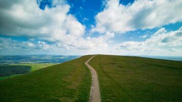 cênico Visão do uma limitar caminho em uma exuberante verde Colina debaixo uma azul céu com nuvens dentro pendle colina, Inglaterra. foto