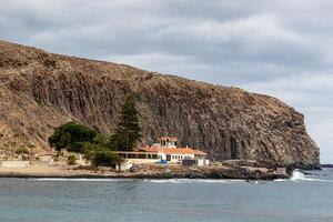 isolado casa de a mar com uma montanha pano de fundo debaixo nublado céu dentro los cristãos, tenerife. foto