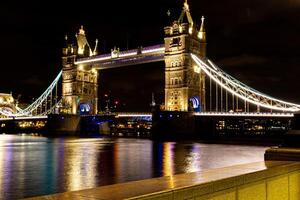 noite Visão do a iluminado torre ponte dentro Londres sobre a Tamisa rio com reflexões em água. foto