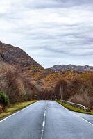 esvaziar rural estrada conduzindo através uma cênico outono panorama com colorida folhagem e montanha pano de fundo debaixo uma nublado céu. foto