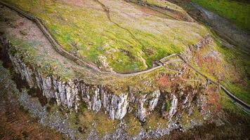 aéreo Visão do uma enrolamento caminho em uma exuberante verde penhasco com rochoso arestas às sicômoro brecha, Northumberlândia, Reino Unido. foto
