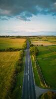 aéreo Visão do uma em linha reta país estrada corte através verde Campos com uma nublado céu acima dentro Iorque. foto