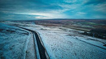 enrolamento estrada através uma Nevado panorama às crepúsculo com uma dramático céu foto