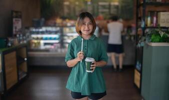 mulher em pé dentro a cafeteria segurando uma beber com uma papel Palha e café xícara, sorrindo e olhando às a câmera, relaxando em férias, estilo de vida conceitos. foto