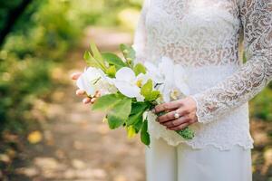 orquídea flor ramalhete dentro a mãos do uma noiva. branco lindo nupcial ramalhete. noiva em pé dentro a jardim segurando uma ramalhete do orquídeas. foto