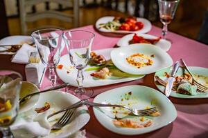 esvaziar sujo pratos, garfos e óculos em a mesa com uma brilhante toalha de mesa dentro a restaurante. sujo comendo equipamentos Incluindo pratos, óculos em mesa depois de jantar. foto