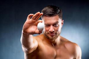musculoso masculino detém uma fresco frango orgânico ovo dentro dele mão e pontos para a Câmera. saudável estilo de vida conceito. foto