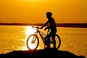 silhueta do uma ciclista com pôr do sol fundo. laranja céu, passatempo, saudável hábitos. foto