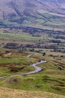 enrolamento estrada através uma montanhoso campo panorama com espalhados árvores e Campos, debaixo uma nublado céu dentro pico distrito, Inglaterra. foto