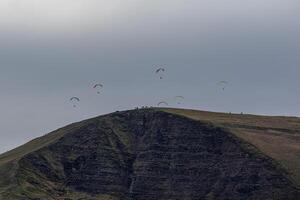 parapentes subindo acima uma montanha cume debaixo uma nublado céu dentro pico distrito, Inglaterra. foto