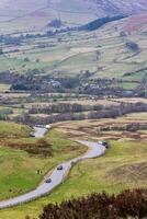 cênico Visão do uma enrolamento estrada através uma exuberante vale com rolando colinas e uma rio, debaixo uma nublado céu dentro pico distrito, Inglaterra. foto