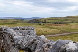 rústico pedra parede com uma borrado fundo do rolando verde colinas e uma Claro céu, representando tranquilo rural panorama dentro pico distrito, Inglaterra. foto
