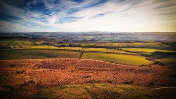 tirar o fôlego panorâmico Visão do uma rolando campo com vibrante Campos debaixo uma dinâmico céu às sicômoro brecha, Northumberlândia, Reino Unido. foto