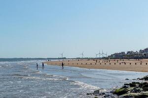 ensolarado paisagem de praia com pessoas passeando e vento turbinas dentro a distância dentro bridlington, Inglaterra. foto