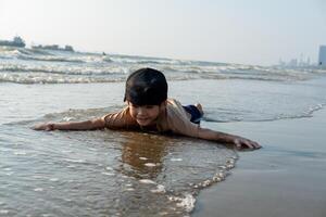 pequeno ásia Garoto jogando dentro a areia às a mar de praia foto