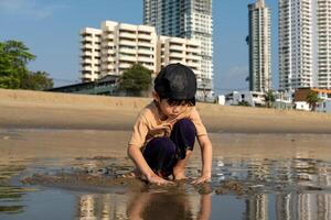 pequeno ásia Garoto jogando dentro a areia às a mar de praia foto