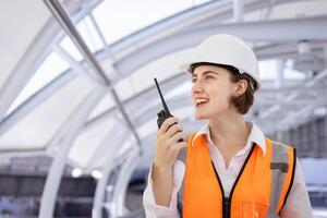 caucasiano mulher engenheiro é usando walkie talkie enquanto inspecionando a construção projeto para moderno arquitetura e real Estado desenvolvimento foto