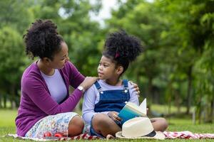 mãe afro-americana está ensinando sua filha a ler enquanto faz um piquenique de verão no parque público para o conceito de educação e felicidade foto