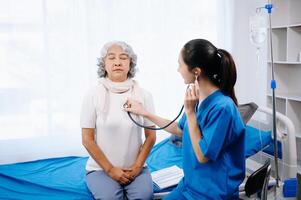 médico e ásia idosos paciente quem mentira em a cama enquanto verificação pulso, consultar e explicar com enfermeira levando Nota dentro hospital enfermarias. foto