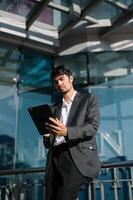 bonito jovem homem de negocios usando uma digital tábua lado de fora a escritório prédio. foto