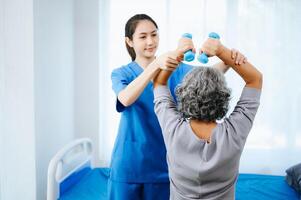 ásia fisioterapeuta ajudando fêmea paciente alongamento braço durante exercício corrigir com haltere dentro mão durante Treinamento mão foto
