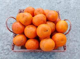 uma vime cesta cheio do fresco laranja frutas em a chão foto