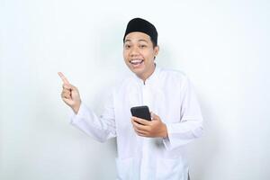 sorridente ásia muçulmano homem apontando para ao lado com segurando Móvel telefone isolado foto