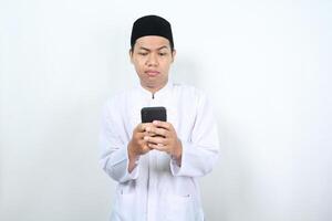 sério muçulmano ásia homem assistindo Móvel telefone com confuso expressão isolado em branco fundo foto